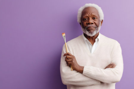 Senior man with a serious expression holding a paintbrush, representing creativity, passion, and artistic endeavorの素材