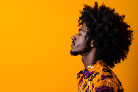 Young man with Afro hairstyle closing eyes, enjoying a moment of peace and calm against an orange backgroundの素材