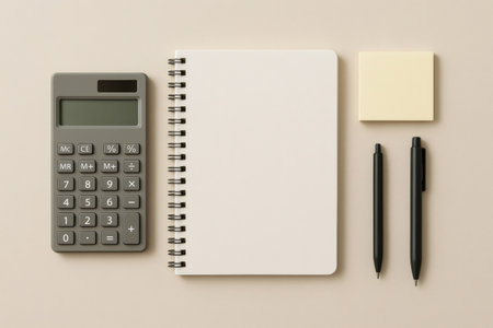 Flat lay showing a calculator, blank spiral notebook, sticky notes, and two pens on a clean, minimalist desk surfaceの素材