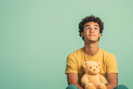 Thoughtful young man looking up, holding a teddy bear. Symbolizing innocence, comfort, development, and future dreamsの素材
