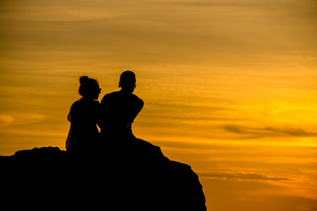 Lovers are sitting on the rocks watching the sunset at the beach.の写真素材