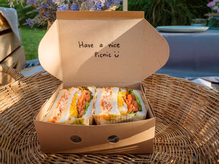 Sandwiches in a basket with a cute message, have a nice picnic. Picnic in a green garden amid...