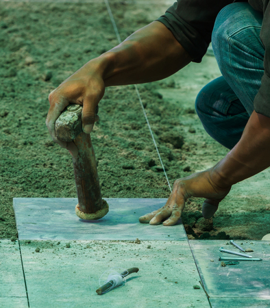 Construction man worker floor tile installation with hammer.の写真素材