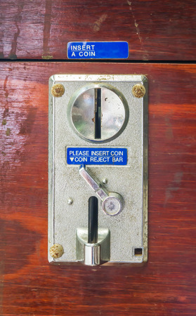 A metal coin slot panel from a coin operated machine on wooden 