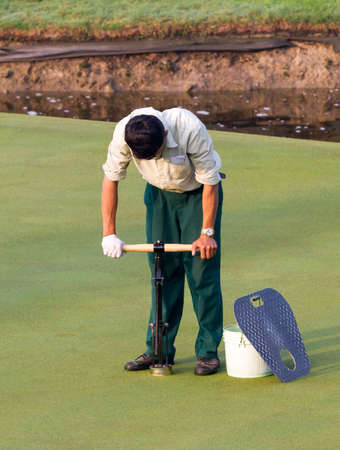 Man worker drill hole on putting green at golf course in the morning.の写真素材