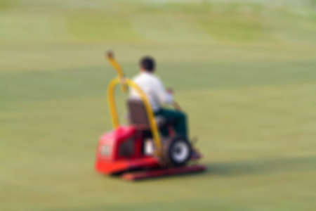 Blur, Man worker driving lawnmover on putting green at golf course in the morning.の写真素材