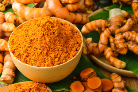 dry turmeric in a wood bowl  with leaf and fresh turmeric on tableの写真素材