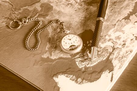 Map book, pens, pocket watch on wood table