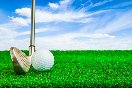 Golf ball and iron on artificial green grass and blue sky backgroundの写真素材