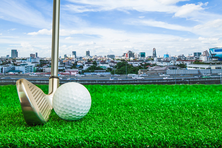 Golf ball and iron on artificial green grass and cityscape backgroundの写真素材