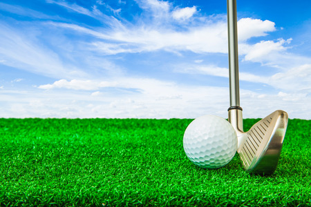 Golf ball and iron on artificial green grass and blue sky backgroundの写真素材