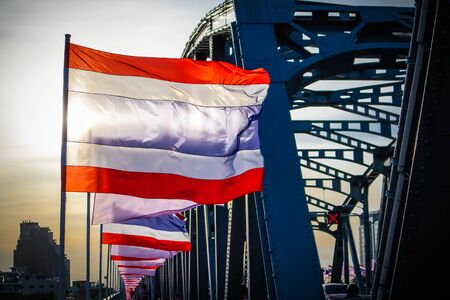 Thai national flag waving in the wind against the sky on Krung Thonburi Bridge at Rajvithi Road Bangkok Thailandの写真素材