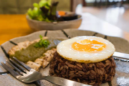 Fried eggs on brown rice and  baked chicken in plates with salad bowls on the table in Thai restaurantsの写真素材