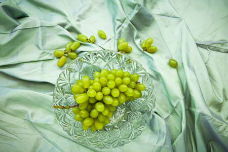 Green grapes in crystal bowl on Thai silk fabric, Natural light background