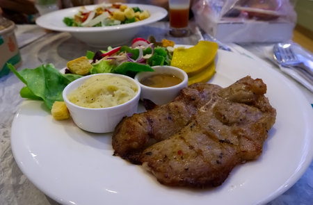 Pork steak and vegetables on white plate on table in restaurant, Bangkok Thailandの写真素材