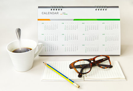 Desk calendar 12 months year 2025 with notepad eyeglasses pencil and hot coffee, object backgroundの写真素材