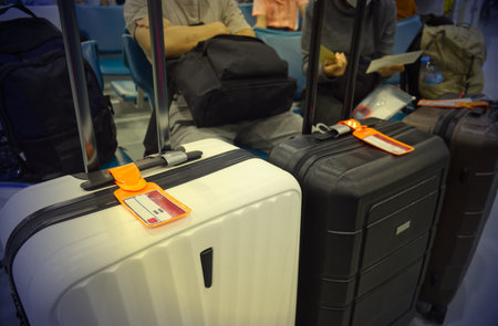 Three suitcases lined up at an airport, each with an orange luggage tag attached to the handle,...