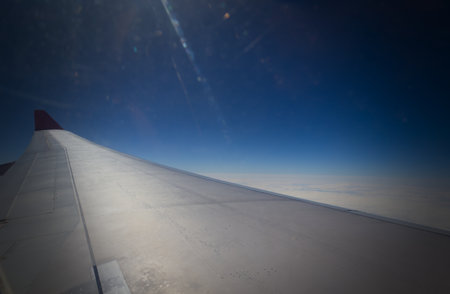 A view from an airplane window showing the aircraft's wing with a red tip, flying high above the sea...