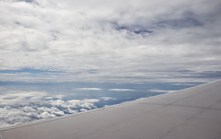 A view from an airplane window showing the aircraft's wing, flying high above the sea under a clear...