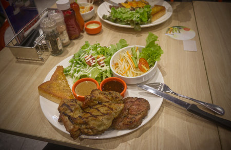 Steak served with toast, salad with spicy dipping sauce and papaya salad in a restaurant in Bangkok