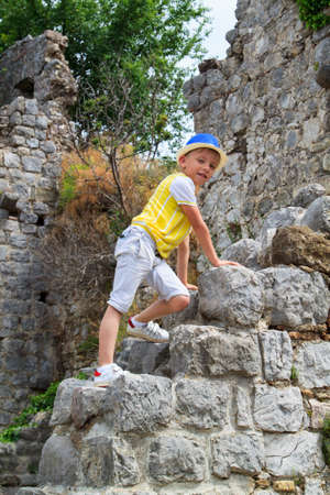 boy in a blue hat sitting on parapet of the ancient fortress of Old town in Budva, Montenegroの写真素材