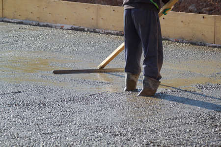 worker in rubber boots stands in uncluttered cement and leveling the surface of the base plate...