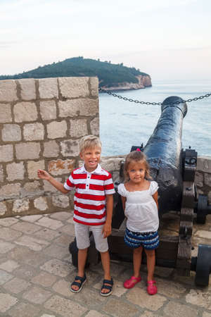 concept of cognitive recreation with children. happy and smiling boy with a girl standing near an old cannon on the city wall enclosing the old town of Dubrovnik, Croatiaの写真素材