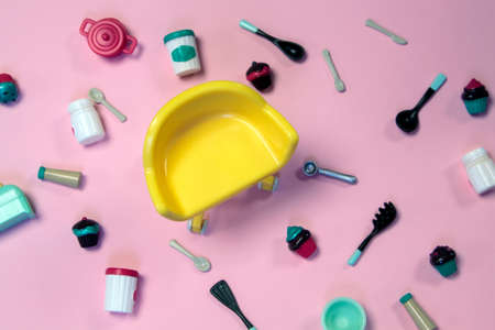 flat lay image of plastic toy tableware with cakes and empty yellow chair on pastel pink backgroundの写真素材