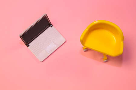Concept of vacant chair. Yellow stool with laptop on pink pastel clean background. Photo in flat lay minimal style.の写真素材