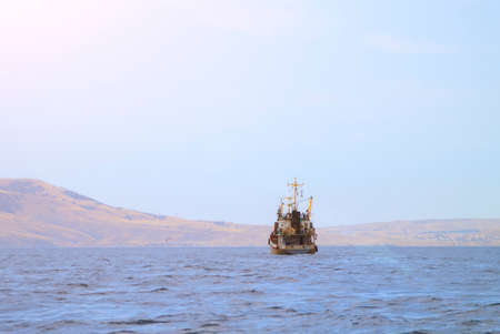 old fishing boat sails along hilly coast and pulls nets