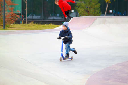 boy on kick scooter trains to ride and perform tricks like older guys in skate park