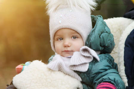 happy baby girl in warm clothes and hat covering his neck from cold wind in autumn outdoor