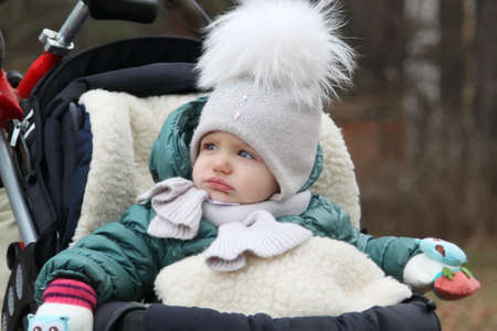 happy baby girl in warm clothes and hat covering his neck from cold wind in autumn outdoorの写真素材