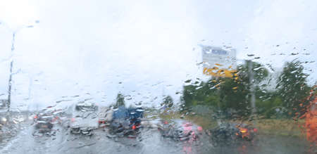 view from car on raindrops on window and road with silhouettes of cars driving behind him in rainy...