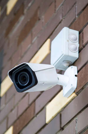 Closed-circuit television camera mounted on brick wall. CCTV security camera outdoors.