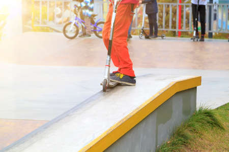 rider on stunt kick scooter slides along metal edge of concrete ramp in skate parkの写真素材