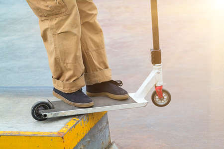 rider on stunt kick scooter slides along metal edge of concrete ramp in skate parkの写真素材