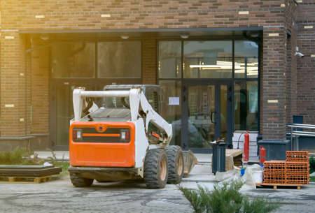 Skid loader stands in front of entrance to new multi-storey house and waits for garbage to be loaded...