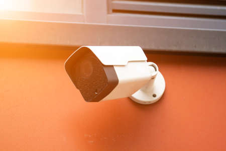 Dirty closed-circuit television camera mounted on orange outdoor wall. CCTV security camera...