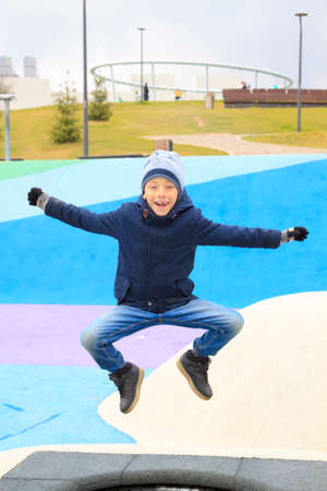 boy in warm clothes jumping on trampoline on modern playground outdoorsの写真素材