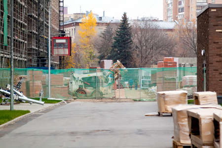small elevator on outside of tower block building structure and mini bulldozer behind fence carries garbage in bucketの写真素材