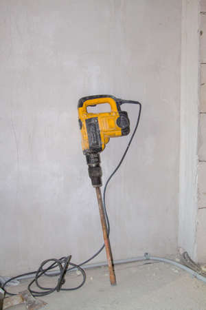 yellow battered large hammer drill (jackhammer or perforator) for interior work is attached to plastered wall in the interior, which is being renovatedの写真素材