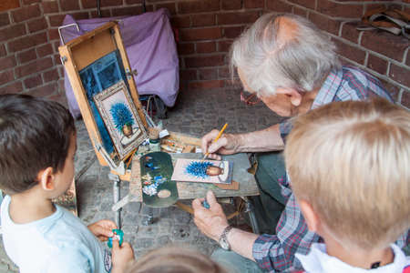 WARSAW, POLAND - June 29, 2018 - children watch as a street artist redraws a bouquet of blue flowers in a potのeditorial素材