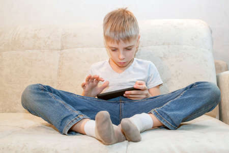 little boy sits at home and plays games on his phone