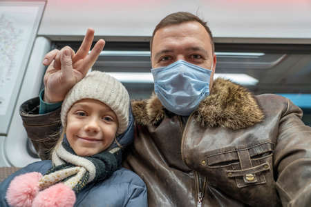 happy father in medical mask with daughter chat online use Web conference, sit in subway train