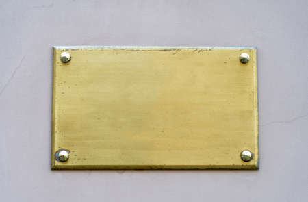 Old yellow metal plate framed and nailed on white stucco wall outdoor backgroundの写真素材