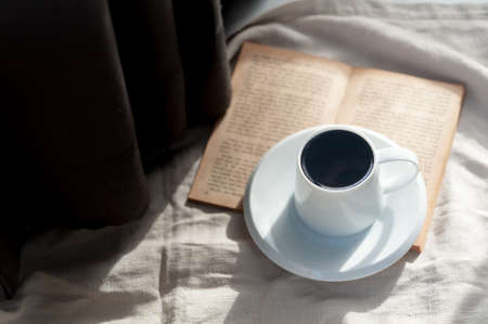 A casual holiday with hot coffee in a white coffee mug put on the book with the warm morning sunshine from the window to feel relaxed good for relaxingの写真素材