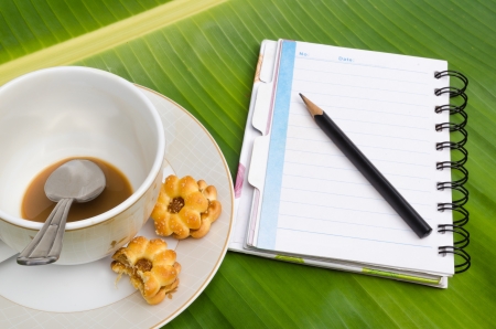notebook and pen with coffee and cookie on banana leaves の写真素材
