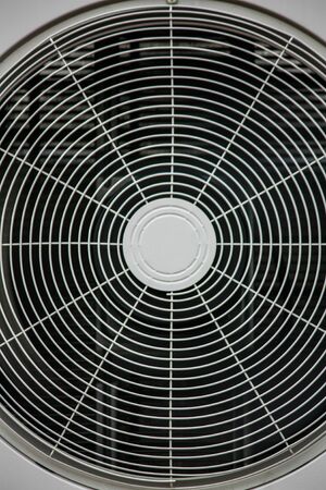 An industrial ventilation fan attached to a building with cage guard