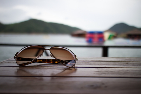 Sunglasses Placed on a wooden floor and Mountain river sky sun Backgroundの写真素材